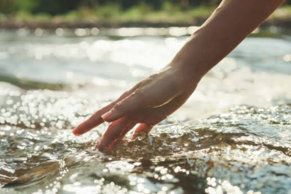 Closeup hand woman touching water in the forest river in vacation with camping at morning. Lifestyle travel nature concept.